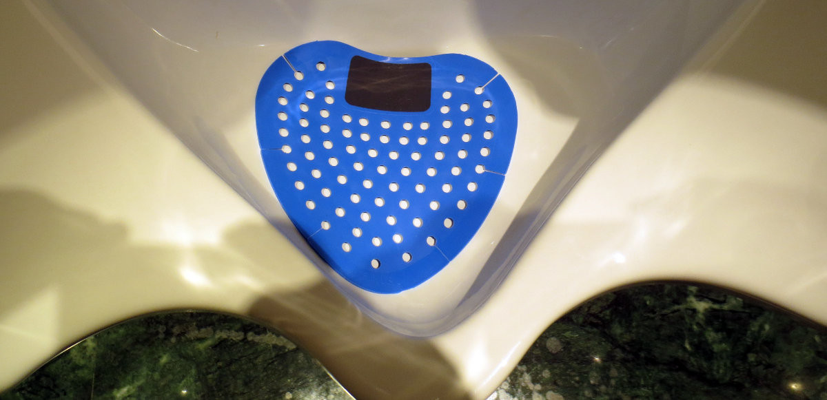 A close up of a pissoir with a blue plastic inlay that has a black patch, where men should ideally direct their beam to.